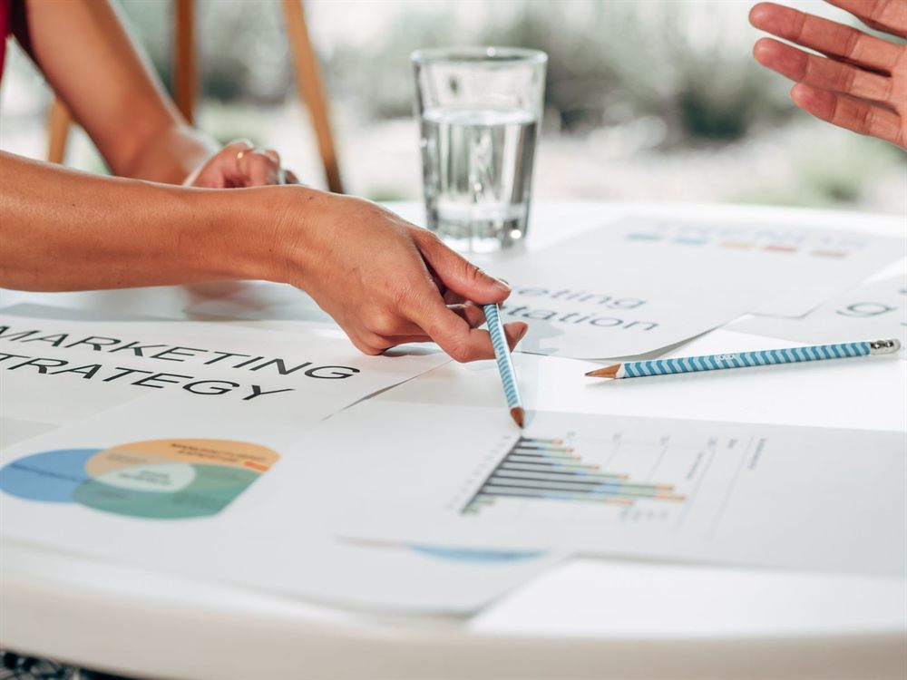 Hands pointing at printed marketing strategy charts on a white table