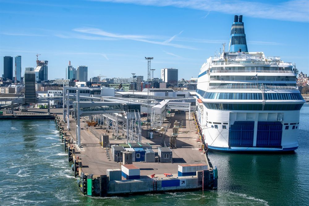 Cruise ship docked at a long pier beside a city waterfront